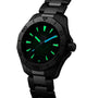A TAG Heuer Aquaracer Professional 200 watch with a black dial, stainless steel case and band, and luminous green markers and hands is displayed at an angle.