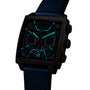 The TAG Heuer Monaco Chronograph, featuring a square black case, skeletonised dial, blue strap, and illuminated blue markers and hands, is displayed against a white background.