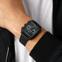 A person wearing a TAG Heuer Monaco Chronograph with a black square face, titanium case, and black strap, paired with a black jacket and white shirt.