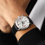 A person wearing a TAG Heuer Special Edition Carrera Chronosprint x Porsche, featuring a silver case, white dial with three subdials, and a black leather strap.