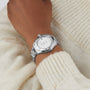 A TAG Heuer Aquaracer 200 Professional Solargraph silver wristwatch with a white face is worn on a wrist over a cream-colored knit sweater.
