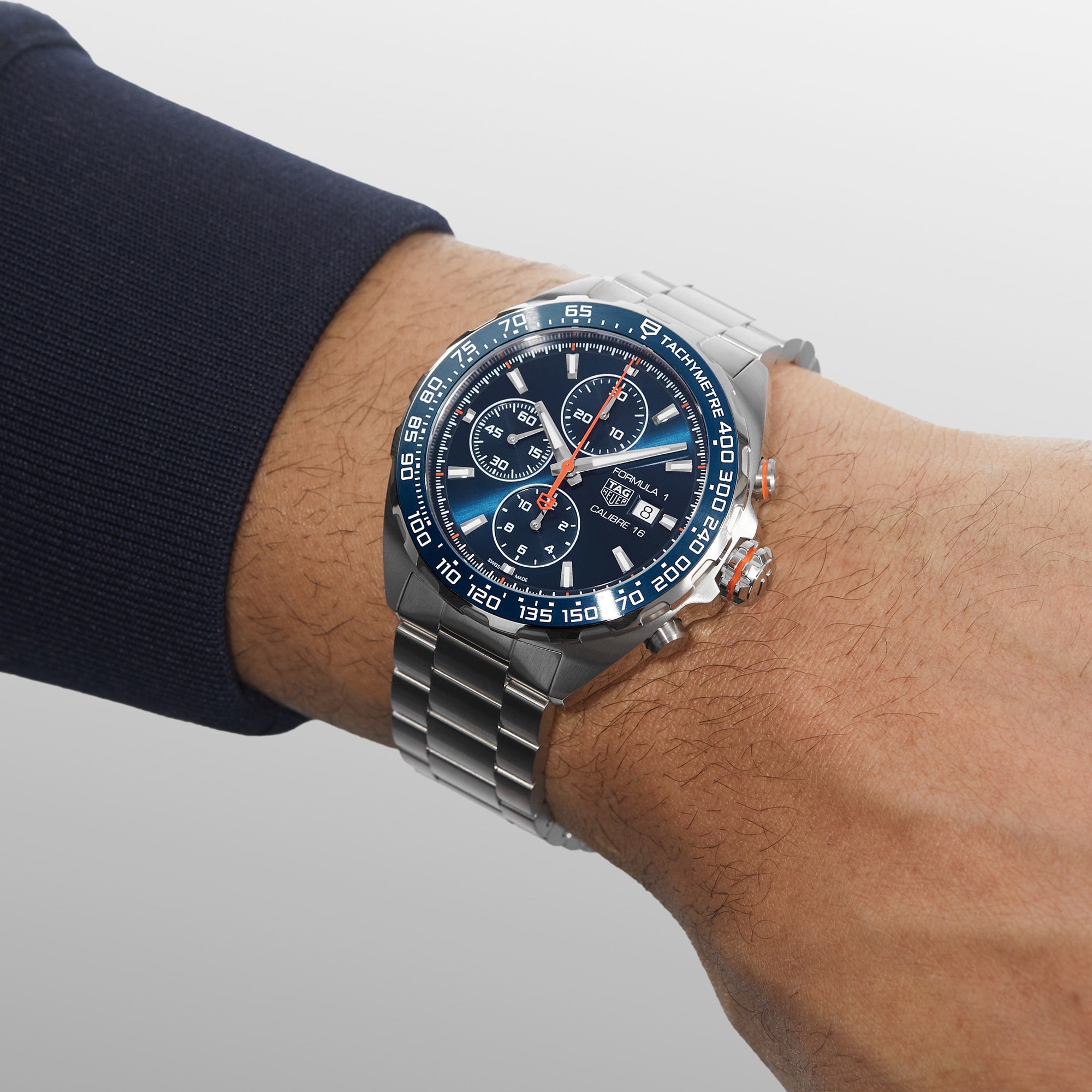 A TAG Heuer Formula 1 Chronograph wristwatch with a blue face, metal band, and blue ceramic tachymeter bezel is worn on a left wrist, showing the time and date.