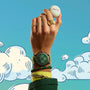 A hand wearing luxury jewelry holds up a TAG Heuer Special Edition Connected Calibre E4 Malbon Golf Edition watch against a sky-blue background with illustrated clouds.