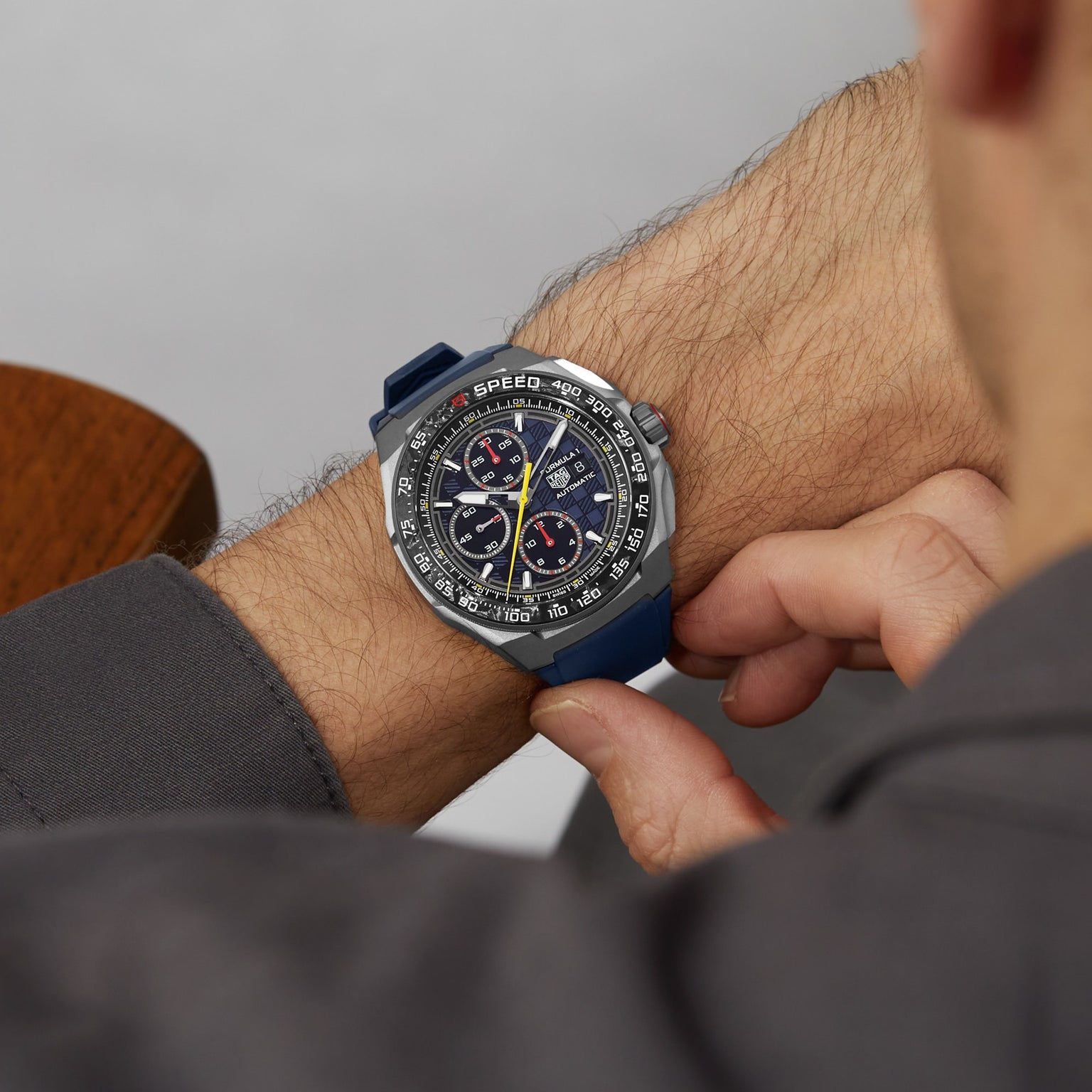 A person in a gray shirt adjusts a TAG Heuer Formula 1 Chronograph X Oracle Red Bull Racing, a motorsport-inspired watch, on their left wrist.