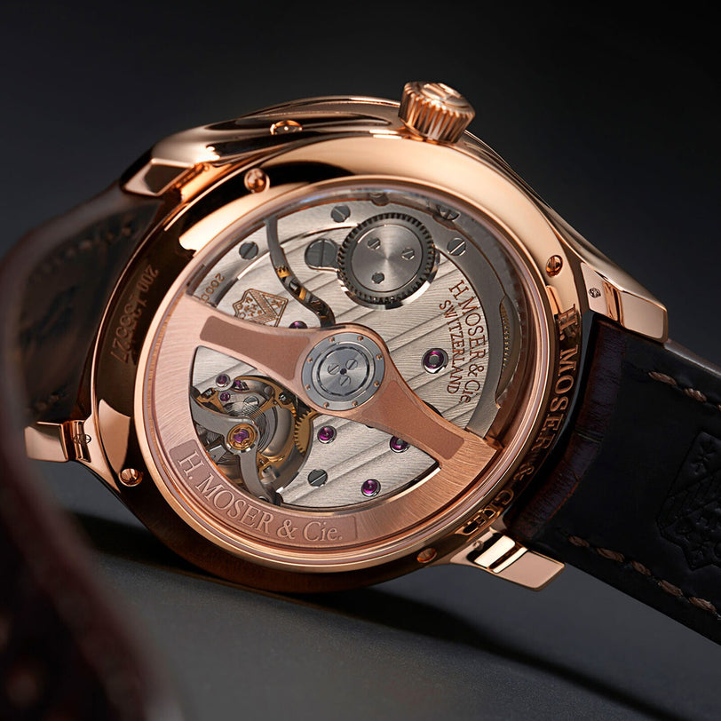 Close-up of the H. Moser & Cie Endeavour Chinese Calendar luxury watch, featuring an exposed rose gold mechanical movement and a brown leather strap.