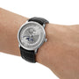 A Blancpain Villeret Quantième Complet silver wristwatch with a black leather band, moonphase dial, and Roman numerals on a persons wrist.