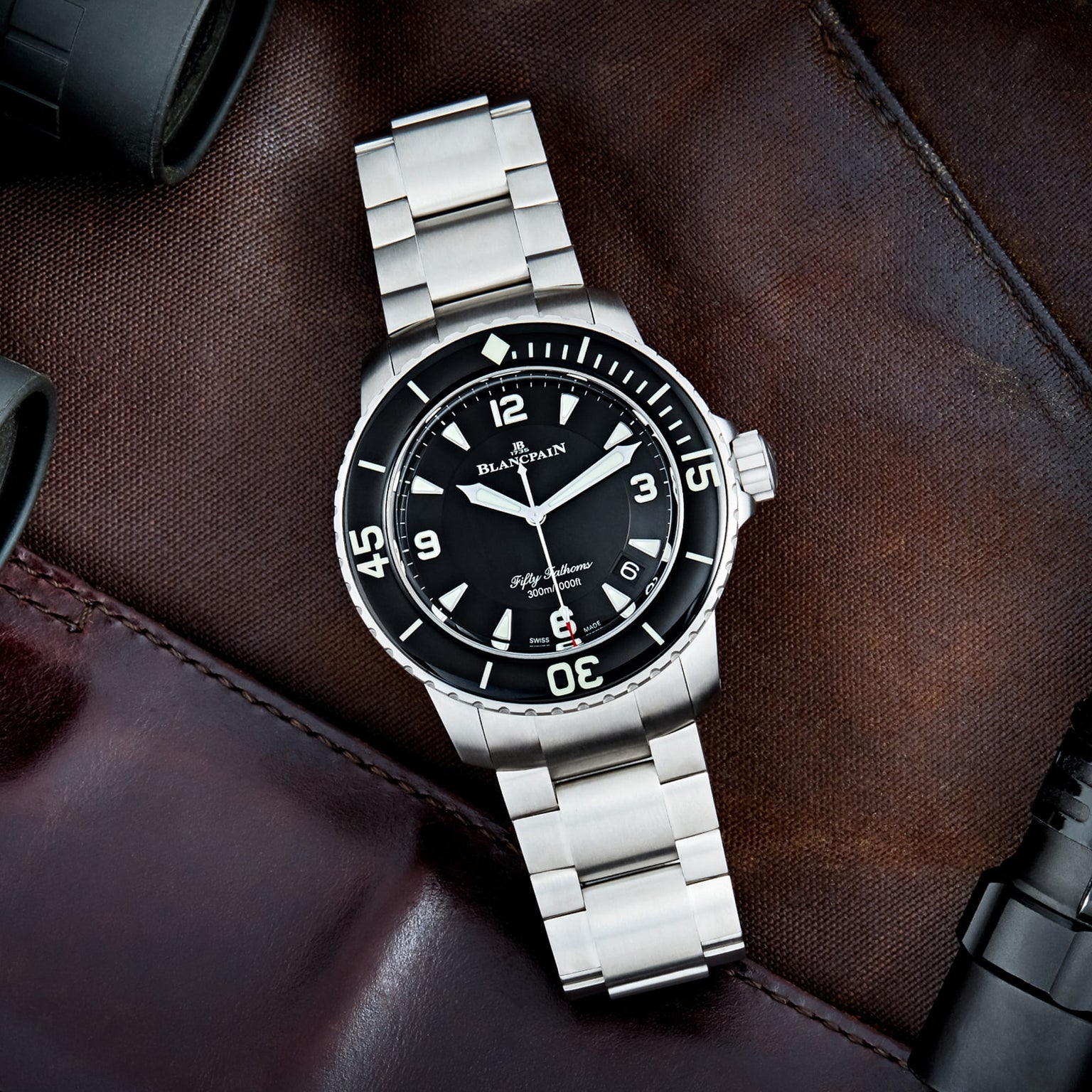 The Blancpain Fifty Fathoms Automatique is a stainless steel diver’s watch with a black dial and bezel, shown on brown leather and also available with a metal bracelet.