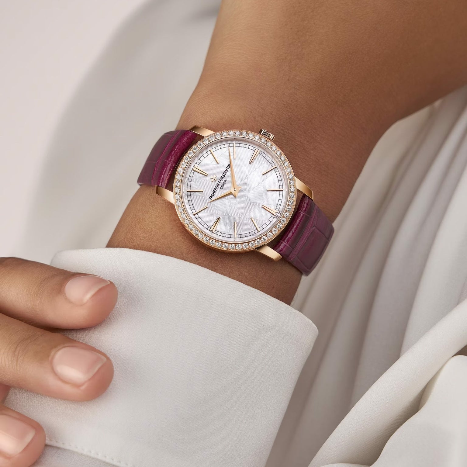 A wrist adorned with the limited edition Vacheron Constantin Traditionnelle Manual-winding 18K pink gold watch, set with diamonds, featuring a white dial and magenta leather strap, worn with a white long-sleeved garment.