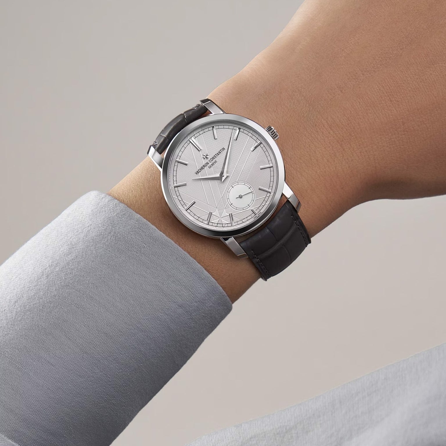 A person wearing a limited edition Vacheron Constantin Traditionnelle Manual-Winding platinum watch with a black leather strap and small seconds subdial on their left wrist.