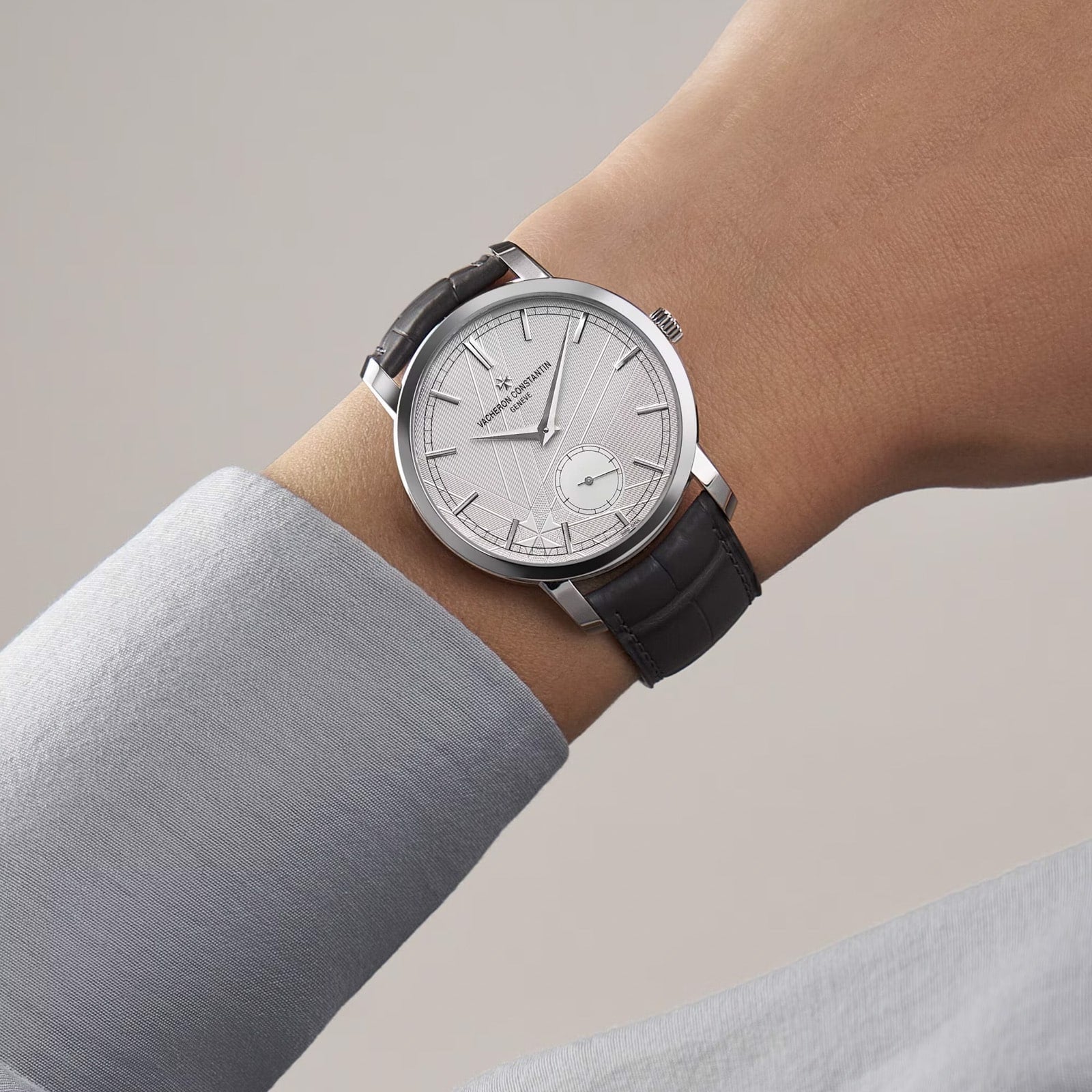 A person wearing a limited edition Vacheron Constantin Traditionnelle Manual-Winding platinum watch with a black leather strap and small seconds subdial on their left wrist.