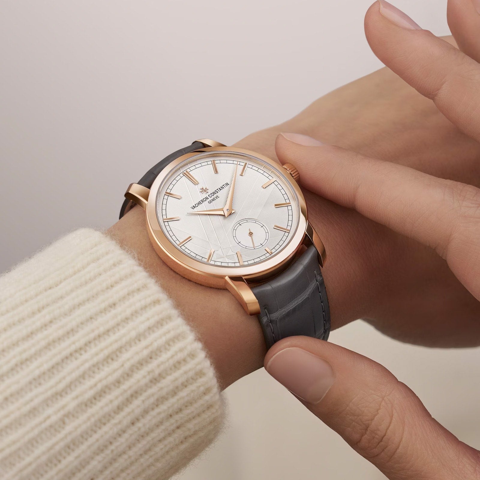 A person wearing a Vacheron Constantin Traditionnelle Manual-winding watch with a gray leather strap and white dial checks the time.