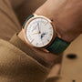 A person dressed in a tan coat wears the Vacheron Constantin Patrimony Moon Phase Retrograde Date, a limited edition gold wristwatch with a green leather strap, featuring moon phase and retrograde date displays.