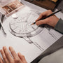 An artist sketches a technical drawing of the Vacheron Constantin Patrimony Moon Phase Retrograde Date watch, referencing its 18K pink gold case and retrograde date display with pencil and watch parts nearby.