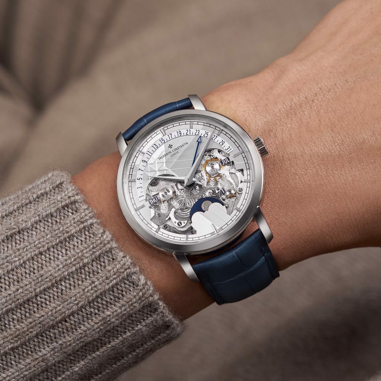 A close-up of a wrist wearing the Vacheron Constantin Traditionnelle Perpetual Calendar Retrograde Date Openface, a platinum timepiece with a blue leather strap, showcasing its skeleton-style design and visible self-winding movement.