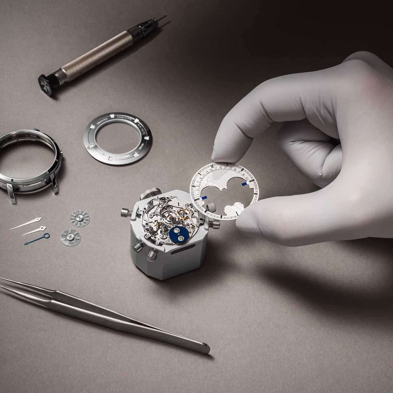 A gloved hand assembles a Vacheron Constantin Traditionnelle Perpetual Calendar Retrograde Date Openface movement on a work surface, surrounded by watch parts, a screwdriver, and tweezers.