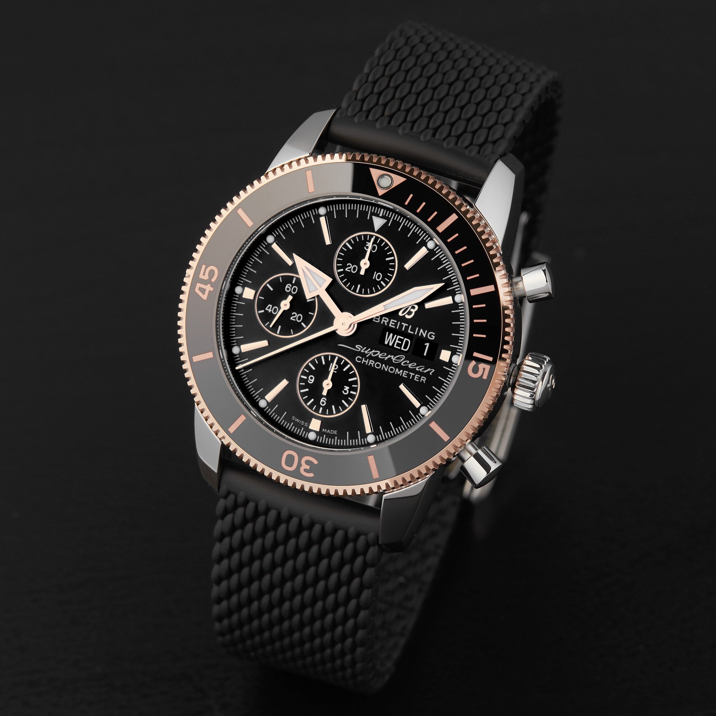 A Breitling Superocean Heritage B20 Automatic 44 in black and rose gold, featuring a high-tech ceramic bezel and black textured strap, is showcased on a dark surface.