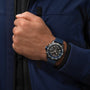 A person in a dark blue jacket wears a Breitling Endurance Pro 44, an athleisure watch with a blue band and multiple dials featuring a SuperQuartz™ chronograph, on their left wrist.