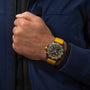 A person in a blue jacket showcases the Breitling Endurance Pro 44, an athleisure watch with a yellow band and black multi-function dial—crafted in Switzerland for precision and sporty style.