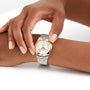 A person with light pink manicured nails fastens a Breitling Chronomat 32 wristwatch, featuring a silver and gold design with a cream-colored face, onto their wrist.
