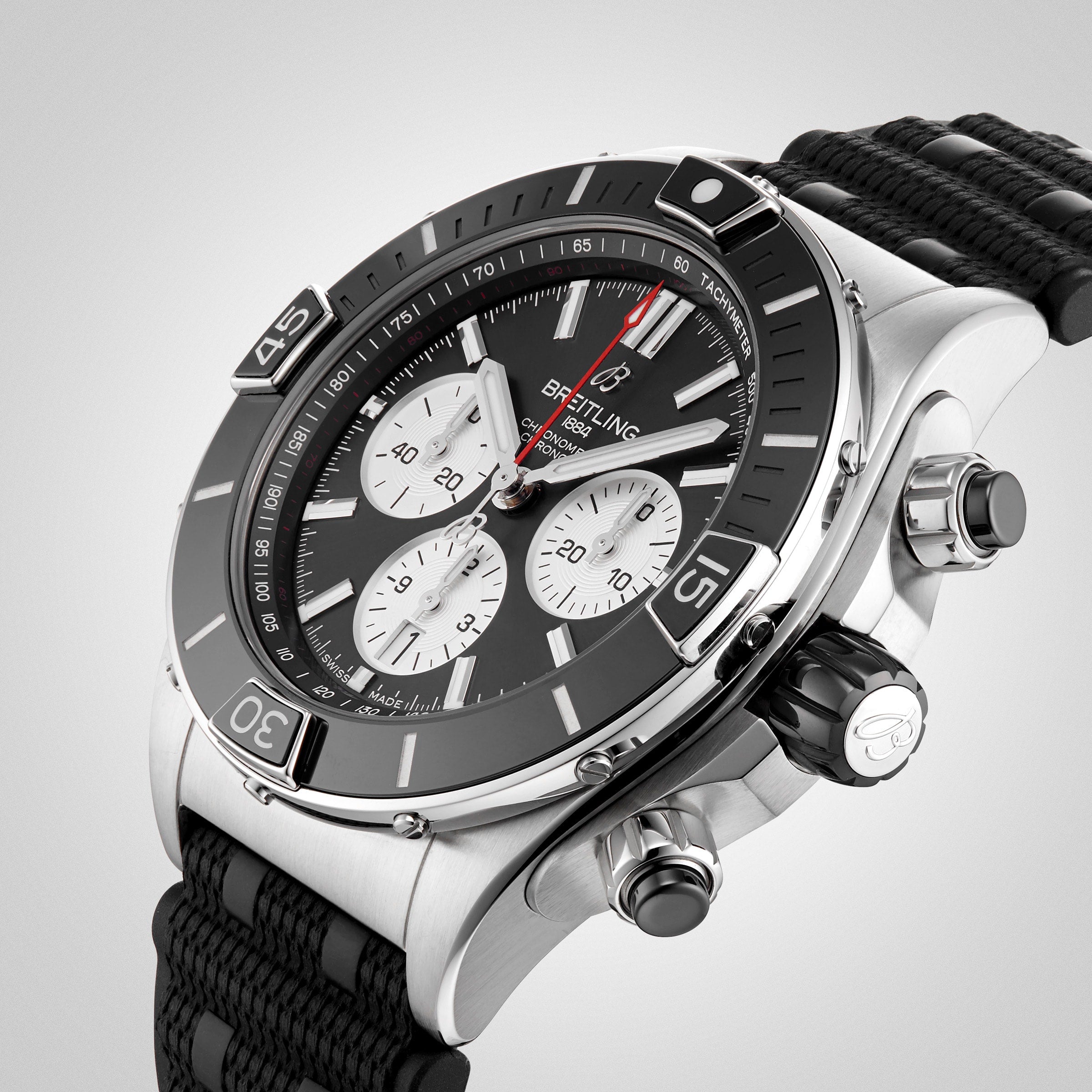 A close-up of a stainless steel Breitling Super Chronomat B01 44 chronograph with a black bezel, three subdials, and a black textured strap, powered by the COSC-certified Breitling 01 calibre.