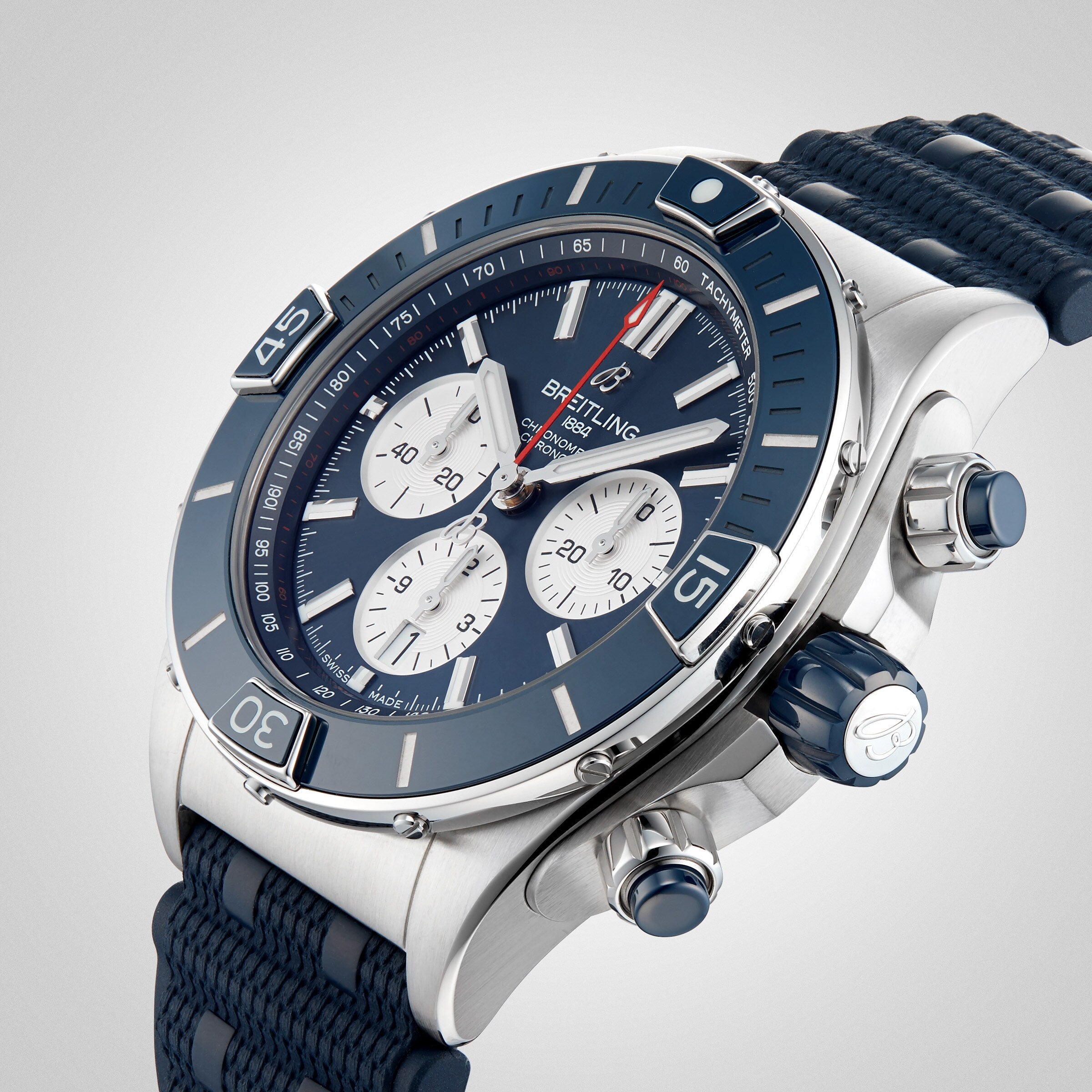 A close-up of the Breitling Super Chronomat B01 44, a stainless steel mechanical chronograph watch with a blue bezel, blue strap, and three white subdials on a blue face.
