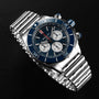 A Breitling Super Chronomat B01 44 stainless steel chronograph wristwatch with a blue bezel, three subdials, and a metal bracelet is displayed on a black surface.