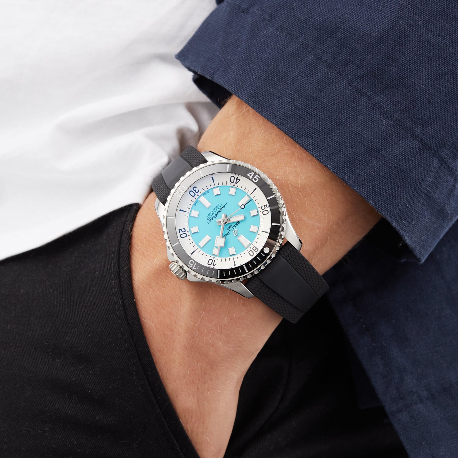 A person with their hand in their pants pocket wears a Breitling Superocean Automatic 44 dive watch featuring a blue dial, stainless steel case, black strap, and silver bezel.