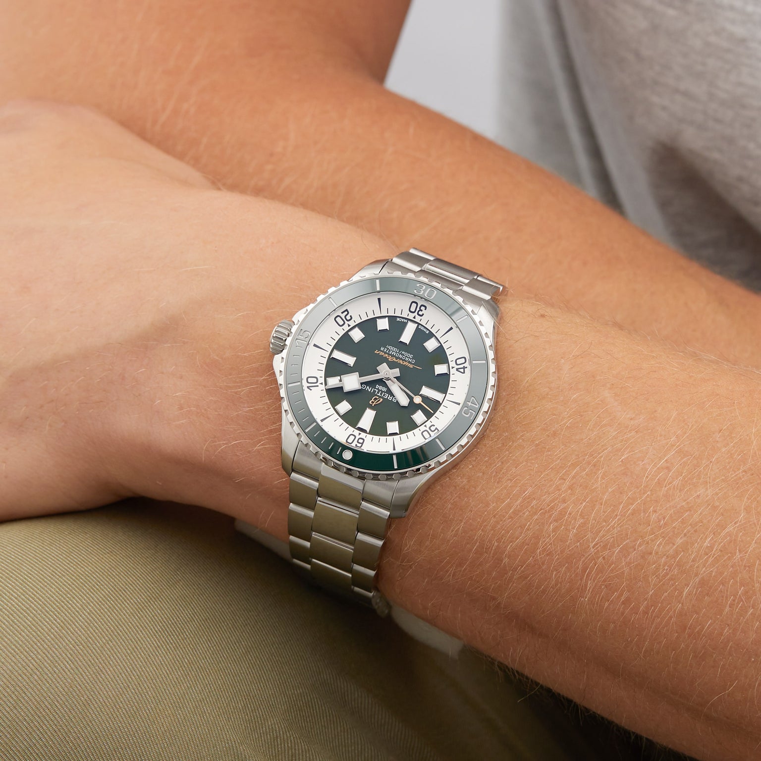 A person wearing a Breitling Superocean Automatic 44 dive watch with a stainless steel case, dark face, silver bezel, and metal link band rests their arm on a light-colored surface.