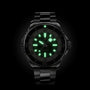 The Breitling Superocean Automatic 46 is a black wristwatch with a metal band, glowing green hour markers and hands on a dark dial, inspired by the iconic 1960s Slow Motion design.