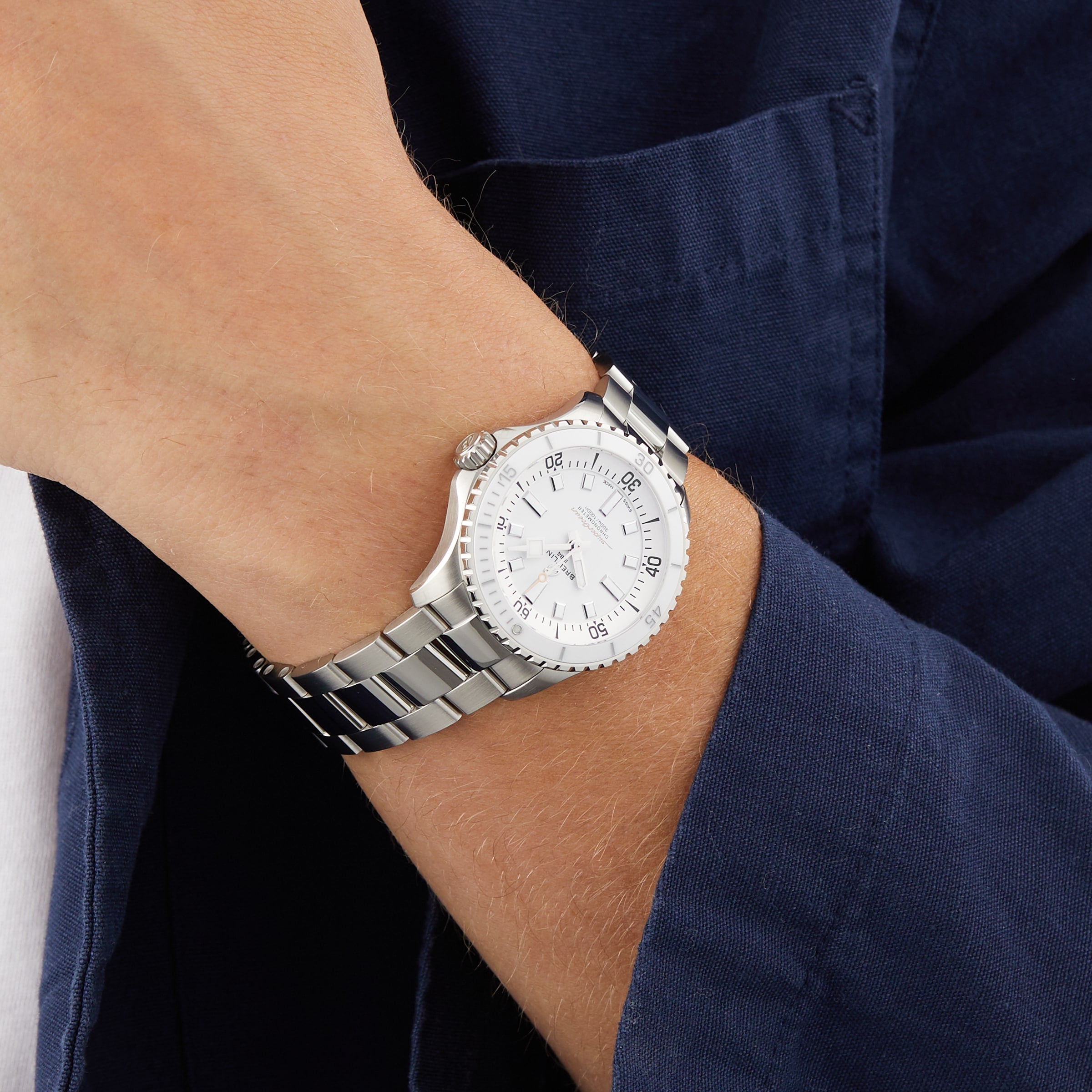 A person wears the Breitling Superocean Automatic 36, featuring a stainless steel case and white dial, paired with a navy blue jacket over a white shirt—embodying classic dive watch style.