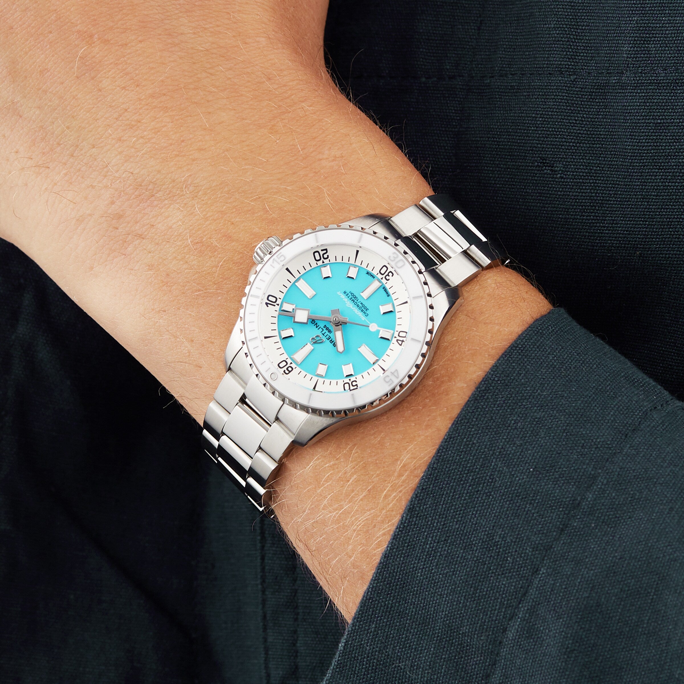 A person wears a Breitling Superocean Automatic 36 diving watch with a silver case, turquoise dial, and silver markers, paired with a dark long-sleeve shirt.