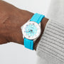 A close-up of a wrist wearing the Breitling Superocean Automatic 36, featuring a silver and turquoise ceramic inlaid bezel and a matching turquoise strap, beside a gray knitted sleeve.