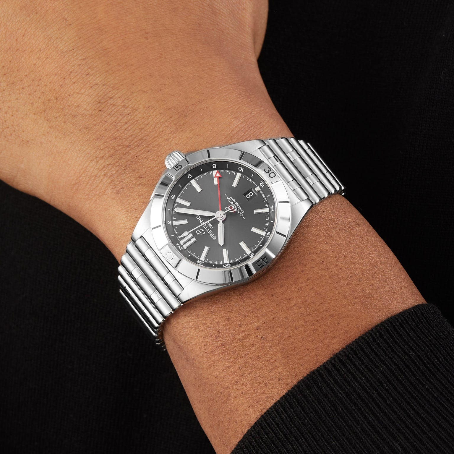 A close-up of a person wearing the Breitling Chronomat Automatic GMT 40, featuring a stainless steel case, black dial, date display, and metal bracelet.