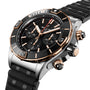 The Breitling Super Chronomat B01 44 is a luxury mechanical chronograph watch featuring a black dial, gold accents, three subdials, a black bezel, and a textured black strap.