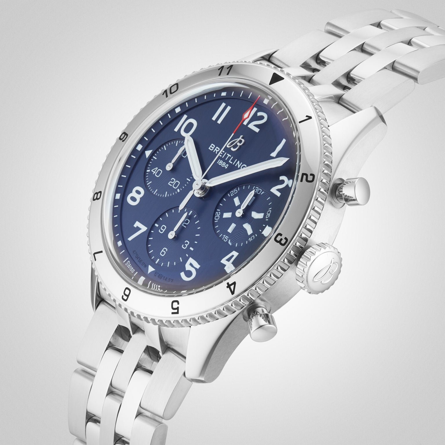 A Breitling Classic AVI Chronograph 42 Tribute To Vought F4U wristwatch with a stainless steel case, blue chronograph dial, silver hour markers, and metal bracelet is displayed at an angle on a white background.