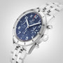 A Breitling Classic AVI Chronograph 42 Tribute To Vought F4U wristwatch with a stainless steel case, blue chronograph dial, silver hour markers, and metal bracelet is displayed at an angle on a white background.
