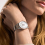 A person with long, light brown hair rests their hand against their cheek, wearing a Breitling Navitimer Automatic 36 wristwatch with a white face and crystal accents.