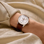 A person wears a Breitling Navitimer Automatic 36 with a mother-of-pearl dial, brown leather strap, and silver case, resting on champagne-colored satin fabric.