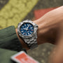 A person in a green jacket wears a Breitling Avenger Automatic GMT 44, featuring a stainless steel case, blue dial, date display, 24-hour bezel, and water resistance.