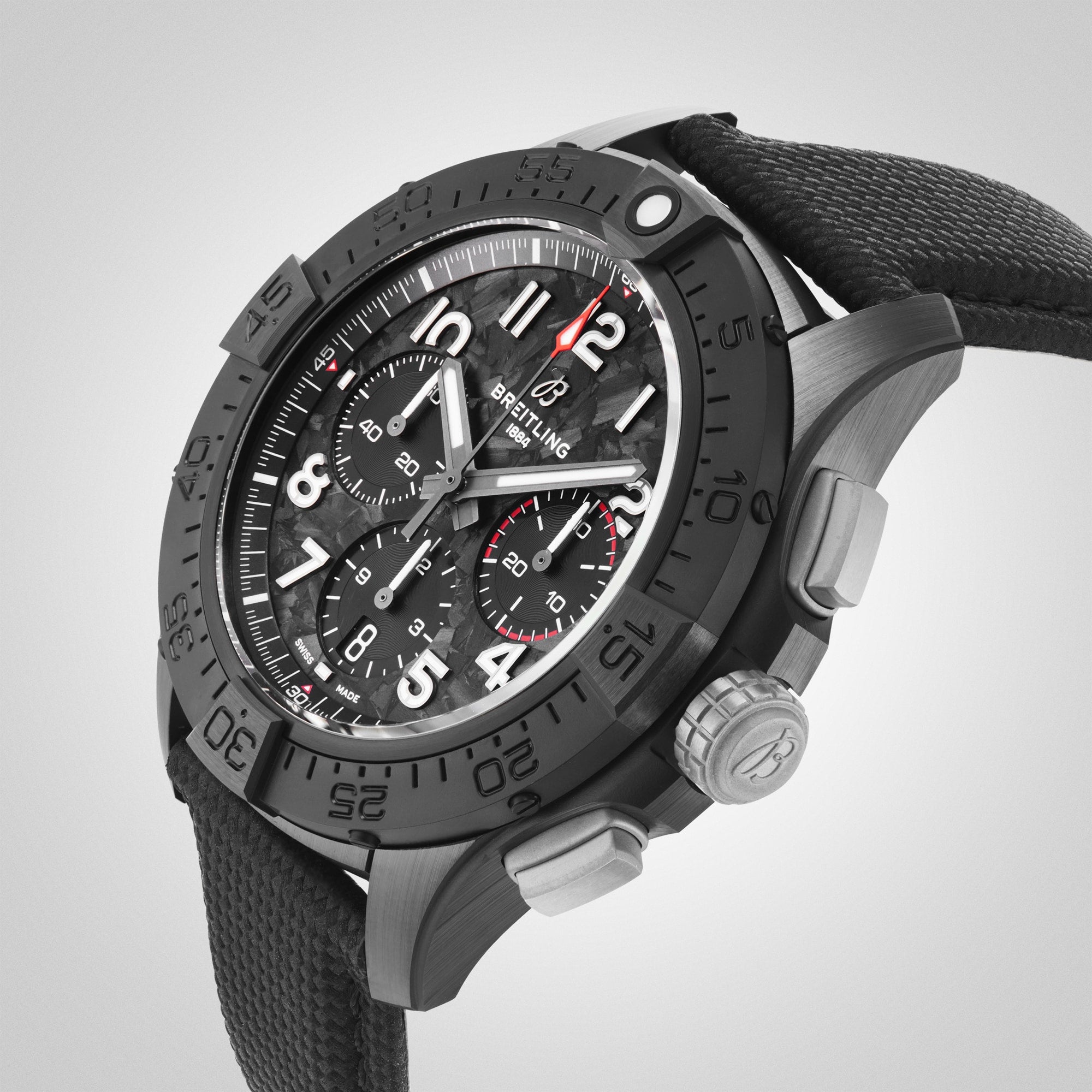 A close-up of the Breitling Avenger B01 Chronograph 44 Night Mission, a black wristwatch with a textured strap, black dial, multiple subdials, and a rotating bezel.
