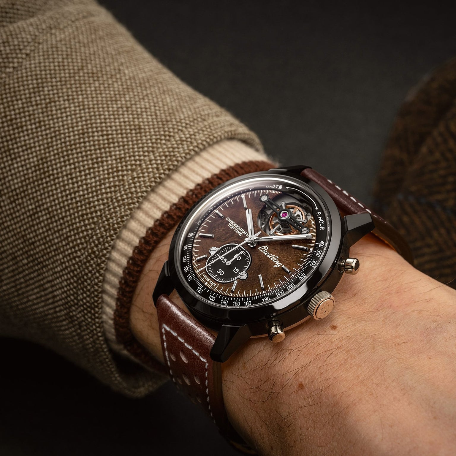 A close-up of a person wearing the Breitling Top Time B21 Chevrolet Corvette—this brown racing chronograph features an open-heart mechanism, brown strap, and peeks from a beige jacket sleeve; ideal for classic sports car enthusiasts.
