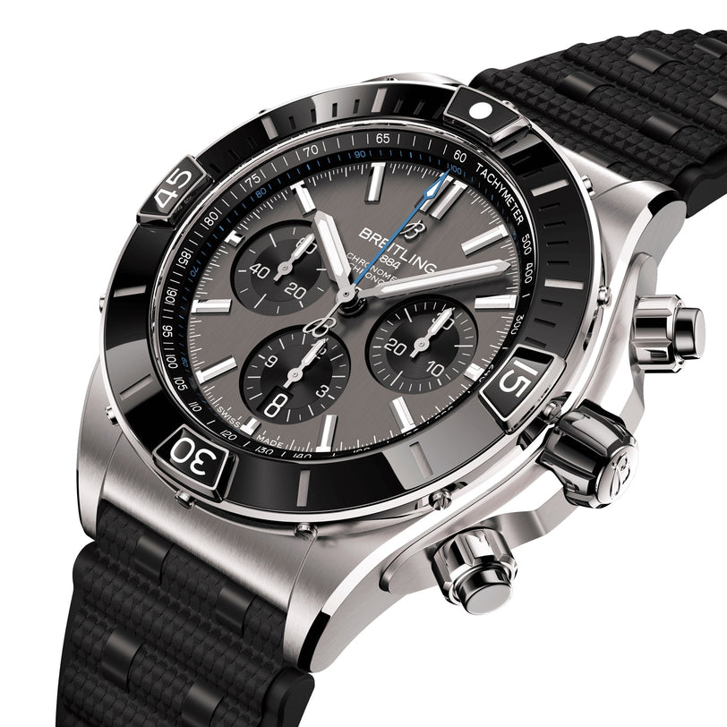 A close-up of the Breitling Super Chronomat B01 44, a stainless steel chronograph with a black bezel, three subdials, tachymeter function, and a textured black rubber strap.