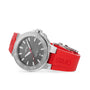 The Oris Aquis Date Relief, a stainless steel divers watch with a grey dial, date display, and red rubber strap, is shown at an angle against a white background.