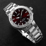 The Oris Aquis Date Relief wristwatch, featuring a stainless steel case, metal bracelet, silver bezel, and striking red dial, is showcased on a black textured surface.