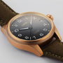 The Oris Big Crown ProPilot Big Date wristwatch features a bronze case, black dial with white numerals, Swiss mechanical movement, date display at 3 o’clock, and an olive green fabric strap.