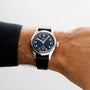 A person wearing an Oris Big Crown Pointer Date Calibre 403 on their left wrist, featuring a black leather strap, black dial with white numerals, and a silver case.
