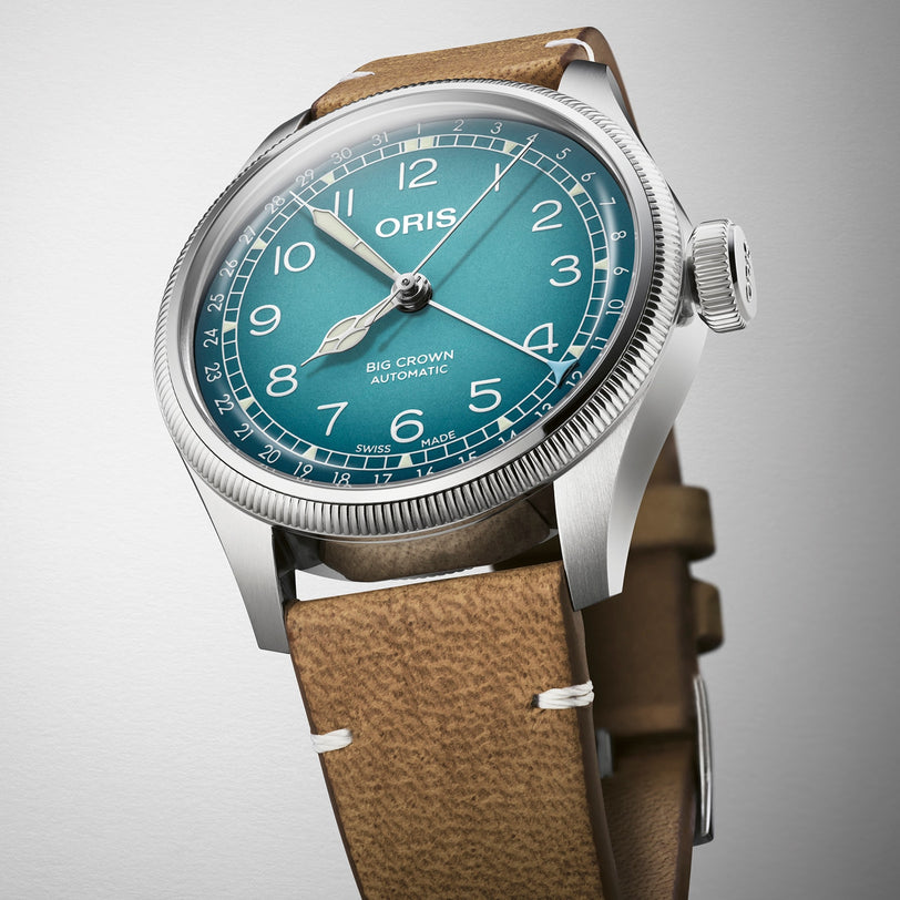 The Oris Big Crown X Cervo Volante is a stainless steel automatic watch with a teal dial, white numerals, and brown leather strap, crafted for professional pilots and presented against a plain background.