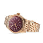 The Oris Big Crown Bronze Pointer Date is shown at an angle, featuring a gold case, burgundy dial with white numerals, and a gold metal link bracelet.