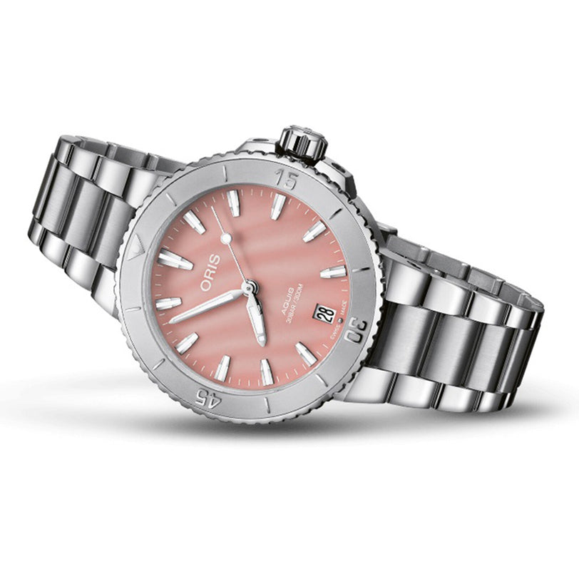 The Oris Aquis Date is a stainless steel diver’s watch with a blush pink dial, white hour markers, date window at 6 o’clock, and a sleek silver metal bracelet.