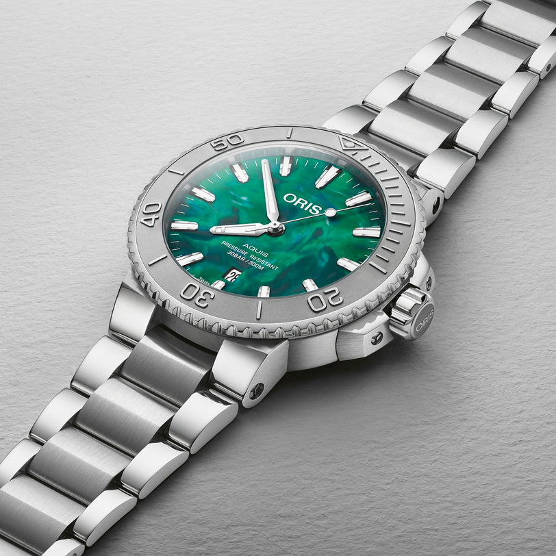 The Oris Aquis Oris X Bracenet is a silver wristwatch with a green mother-of-pearl dial and a matching silver metal bracelet.